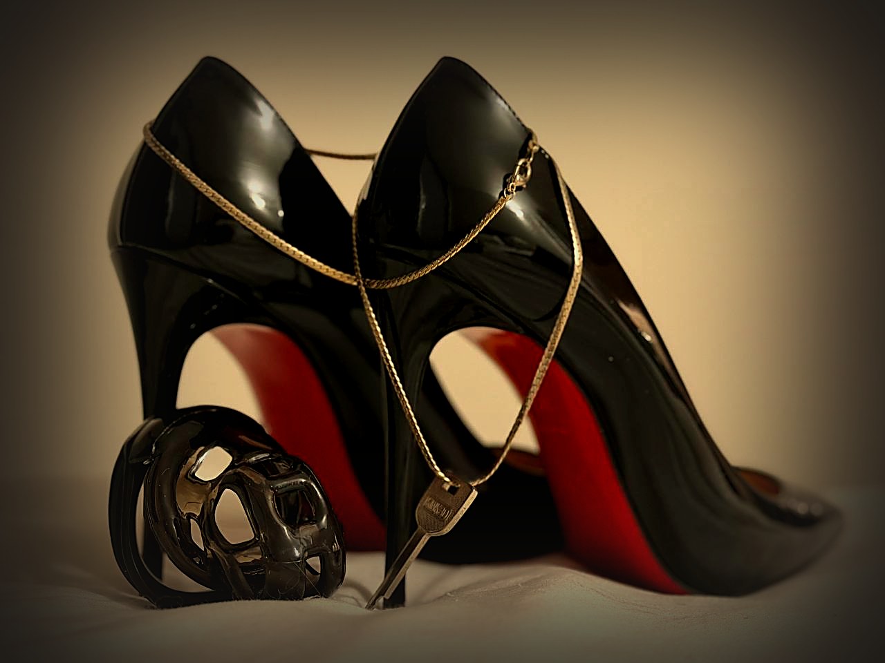 Chastity and keyholding in Sydney: Mistress Katya Green's key on a gold chain draped over black stiletto heels beside a black chastity cage